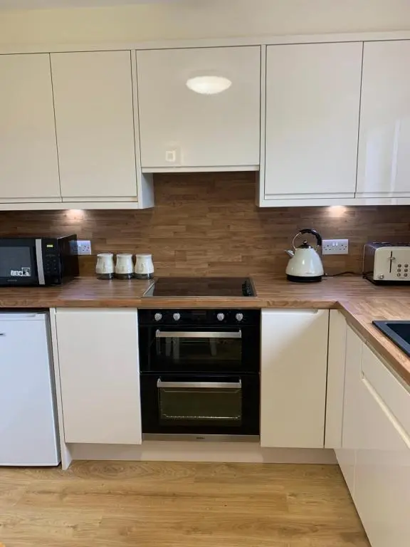 a kitchen with white cabinets and a black oven at Greenfield Cottage in Thrumster