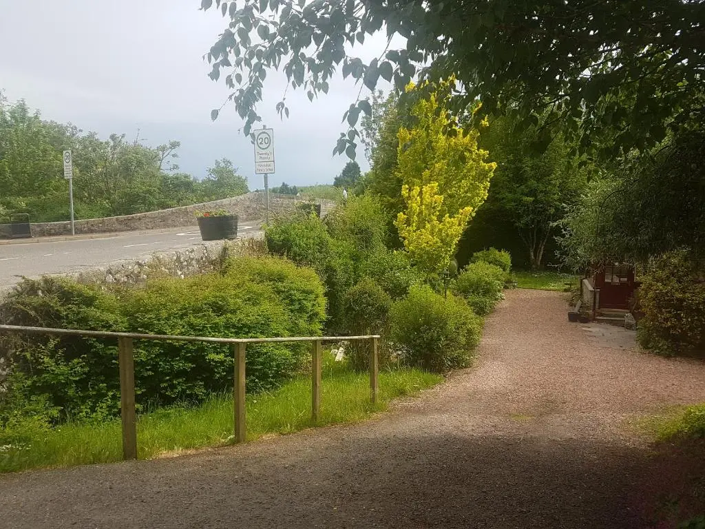 a dirt road with a fence next to a street at Smithy Cottage in Kirkmichael