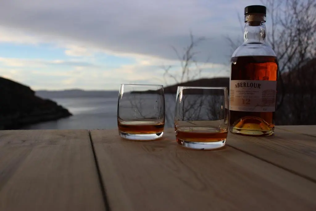a bottle of whisky and two glasses on a wooden table at Tigh na Mara in Ullapool