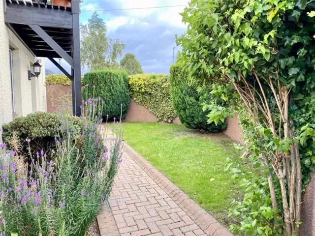 a garden with bushes and purple flowers and a brick walkway at Wellingtonia Court Apartment in Inverness