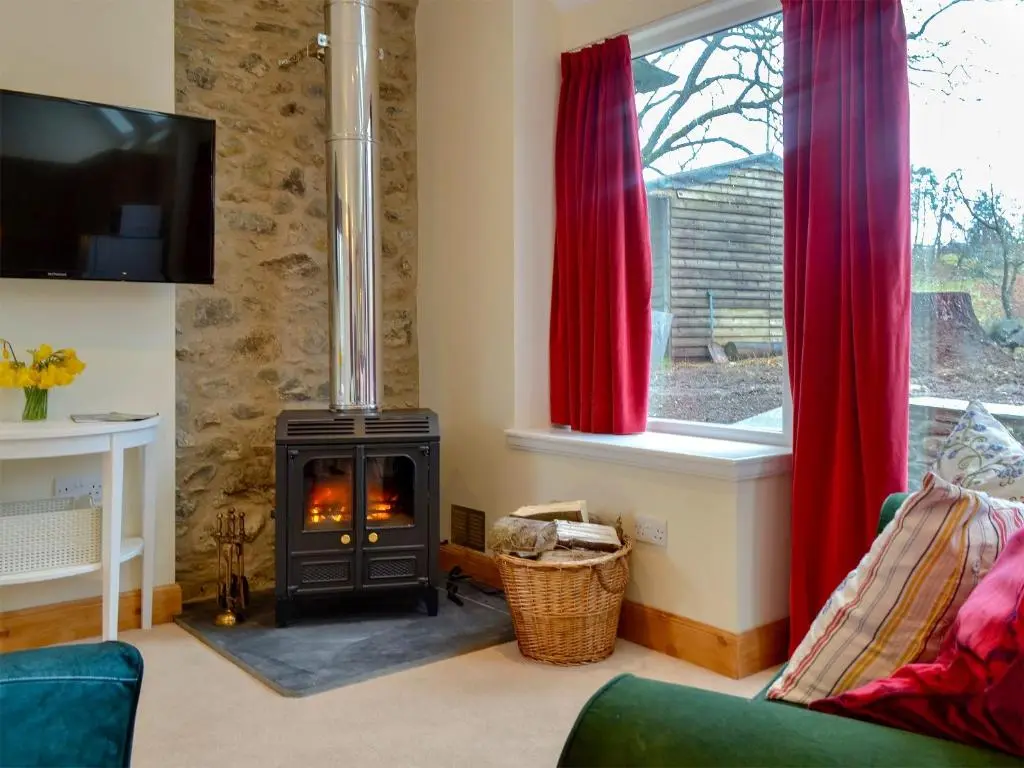 a living room with a wood stove in front of a window at The Old Inverchroskie Kennels in Enochdhu
