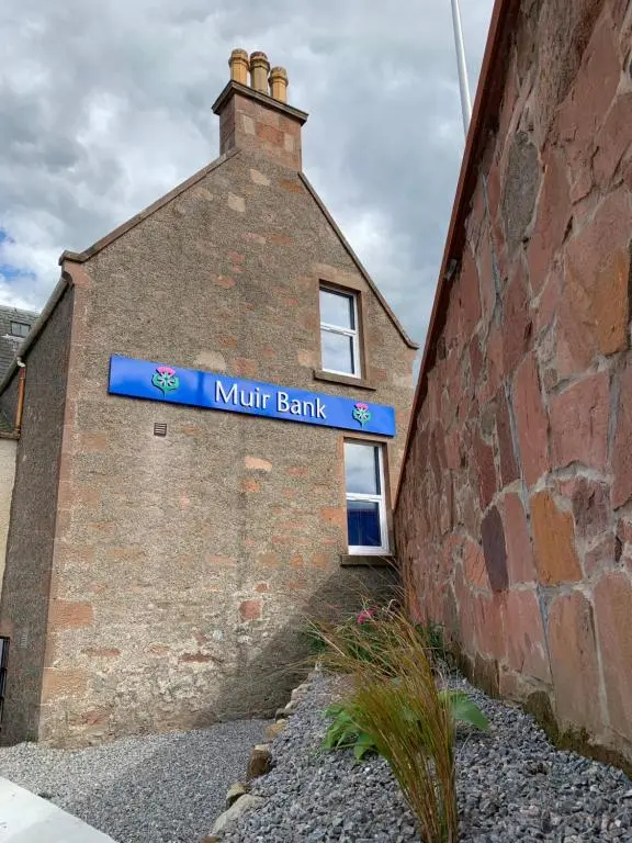 a brick building with a blue sign on it at Muir Bank in Muir of Ord