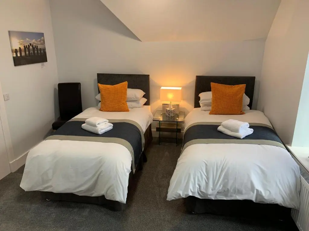 two beds with orange and white pillows in a room at Muir Bank in Muir of Ord