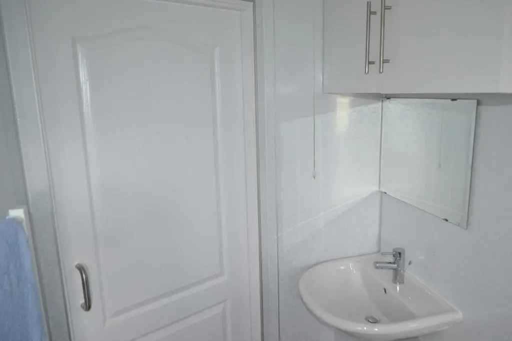 a white bathroom with a sink and a cabinet at Kirkside Holiday Home in Alness