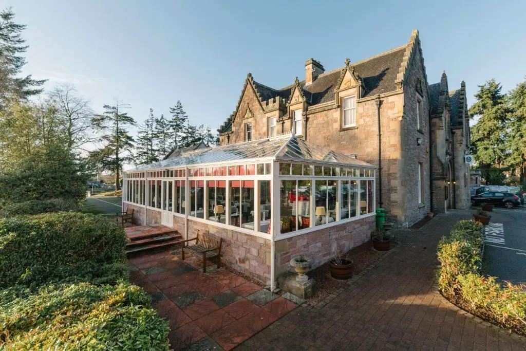 an old house with a greenhouse in front of it at Inverness Lochardil House, by Highland Coast Hotels in Inverness