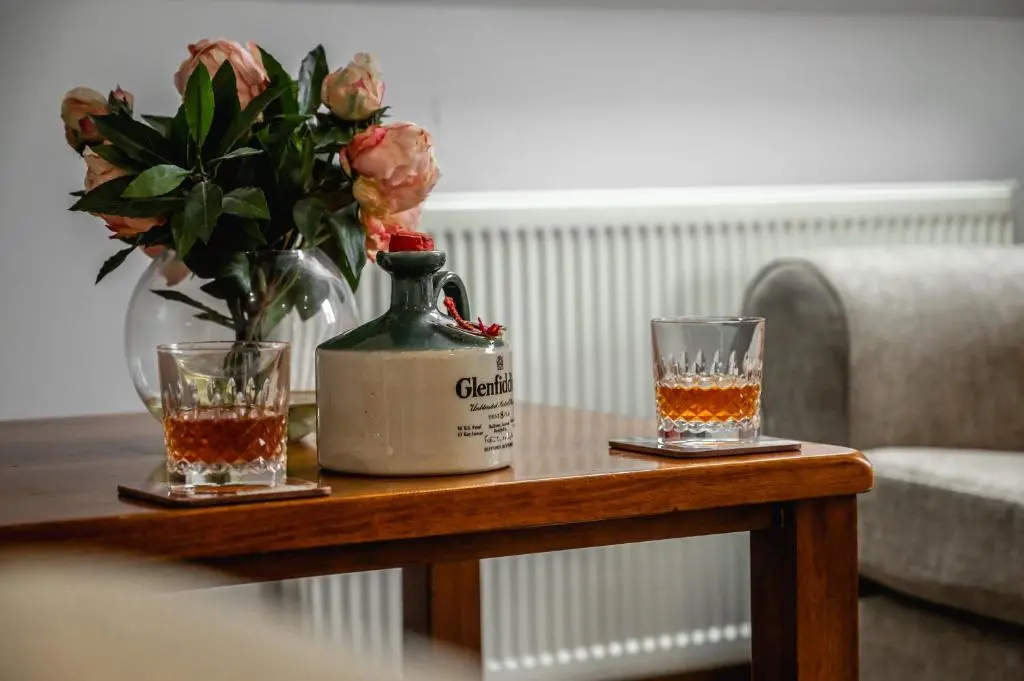 a table with two glasses and a bottle and a vase with flowers at Aldo's Place in Dingwall