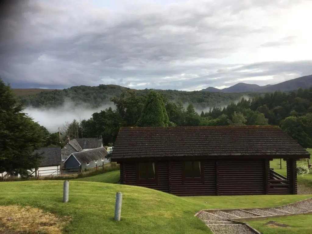 a log cabin in a field with mountains in the background at Highgarry Lodges in Invergarry