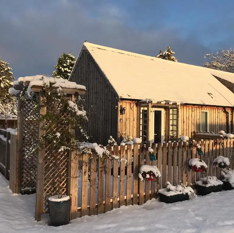 a wooden fence in front of a house covered in snow at Courtyard Bothy in Grantown on Spey