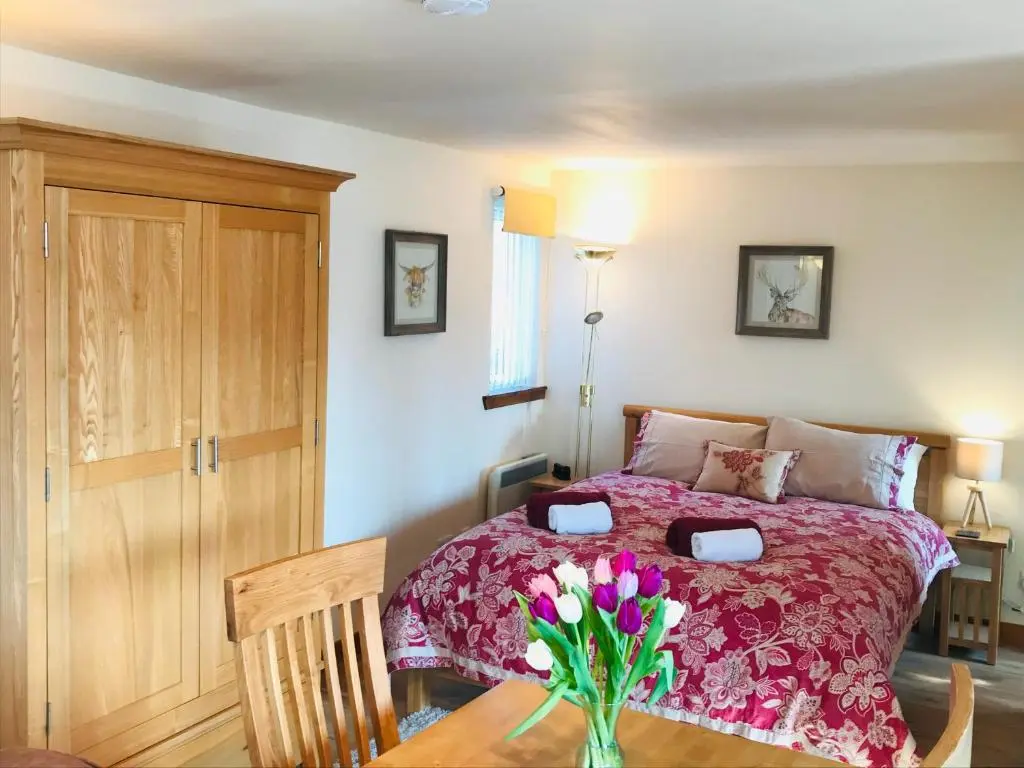 a bedroom with a bed with a vase of flowers on a table at Courtyard Bothy in Grantown on Spey