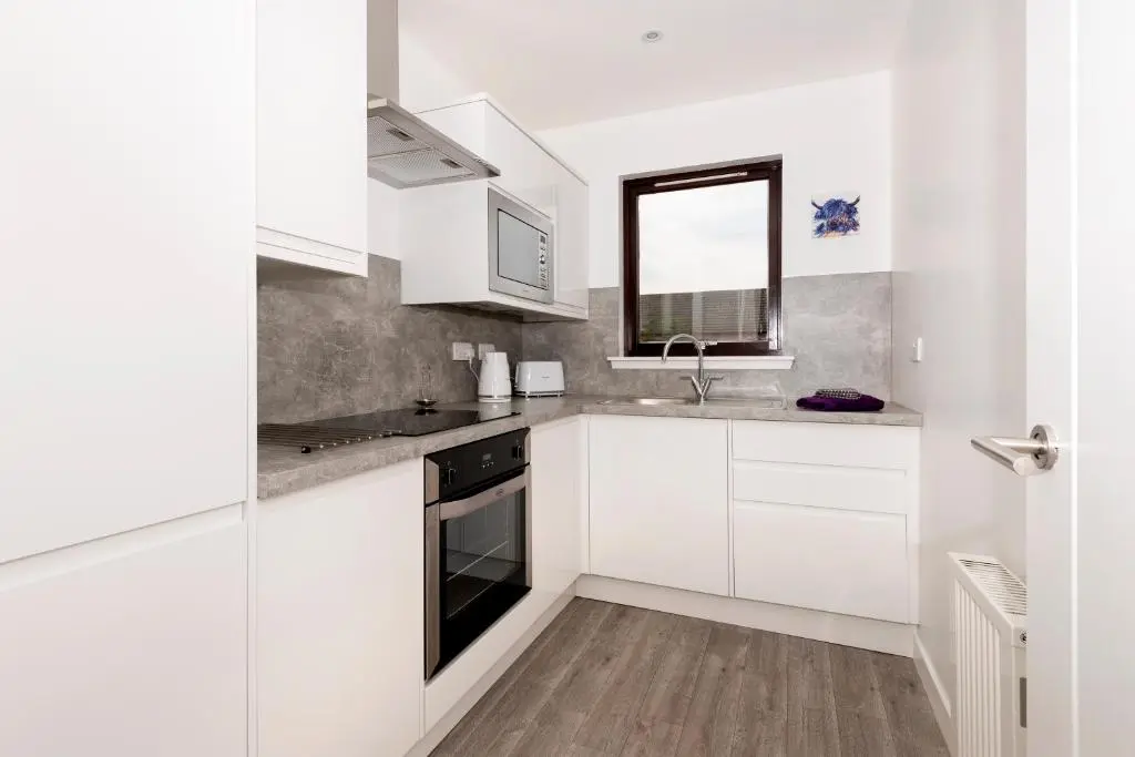 a white kitchen with white cabinets and a window at No. 6 Apartment in Inverness