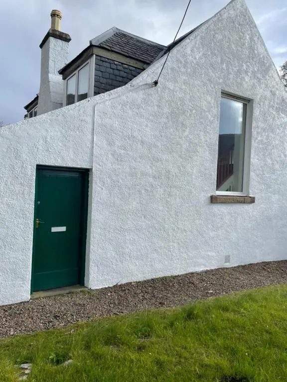 a white building with a green door and a window at Inverlael Farm Cottages in Inverlael
