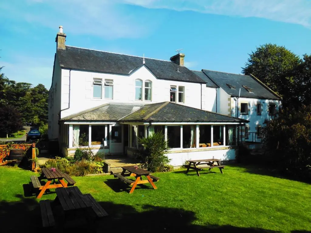 a large white house with picnic tables in the yard at Morag's Lodge in Fort Augustus