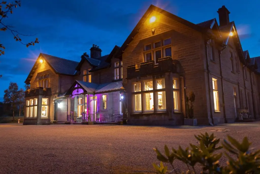 a large house with lights on the front at night at Ledgowan Lodge Hotel in Achnasheen