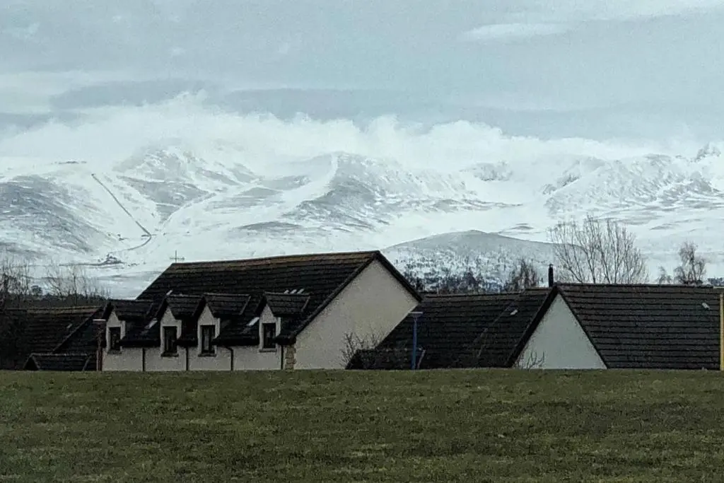 a group of houses with snow covered mountains in the background at Stelvio in Aviemore