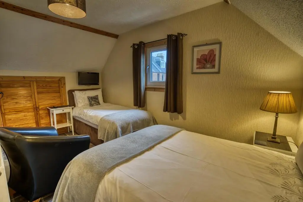 a room with two beds and a chair and a window at Pitfaranne Guest House in Inverness
