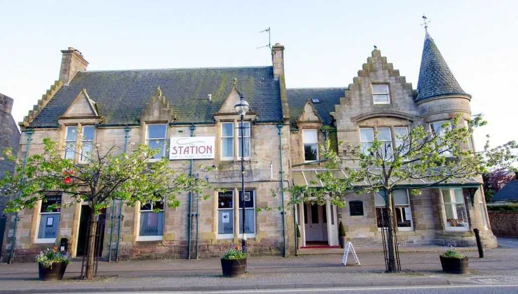 an old stone building with trees in front of it at The Station Hotel in Alness