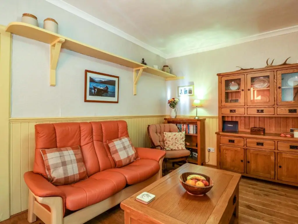 a living room with an orange couch and a table at The Bothy in Kirriemuir