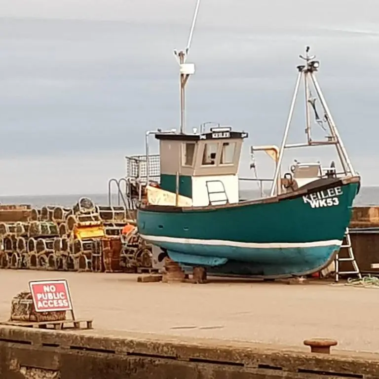 a green boat is sitting on the beach at Helmsdale Lodge Hostel - all rooms en-suite in Helmsdale
