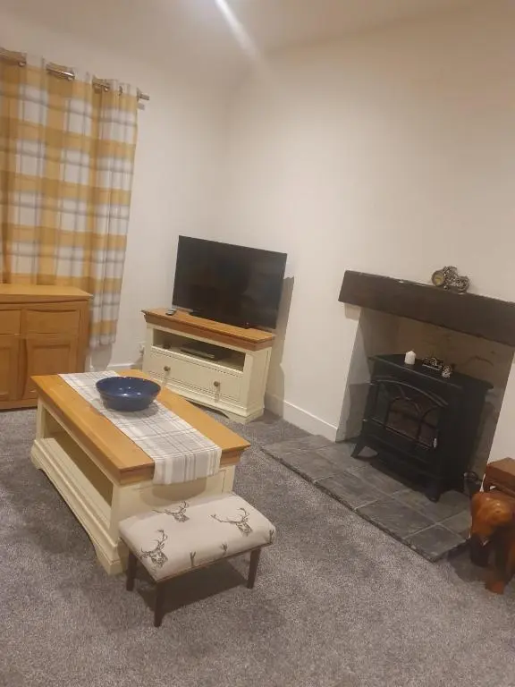 a living room with a tv and a table and a fireplace at Delny Muir House in Invergordon