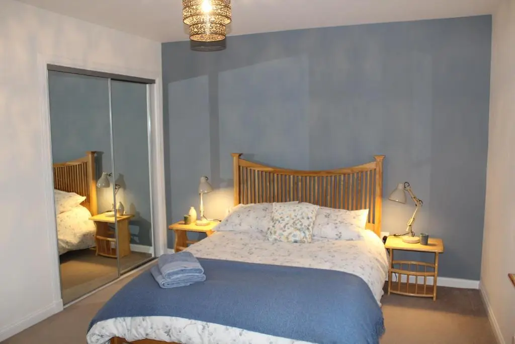 a bedroom with a bed with a blue blanket and a mirror at Roualeyn in Huntly