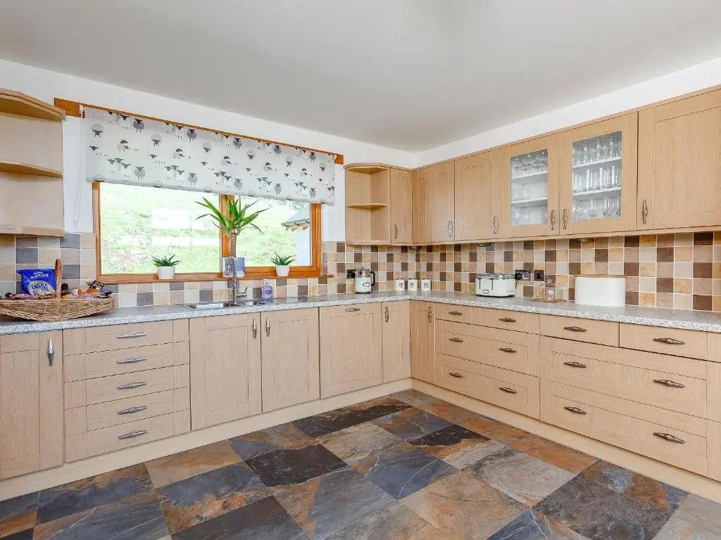 a large kitchen with wooden cabinets and a window at Sunnyside House in Duthil