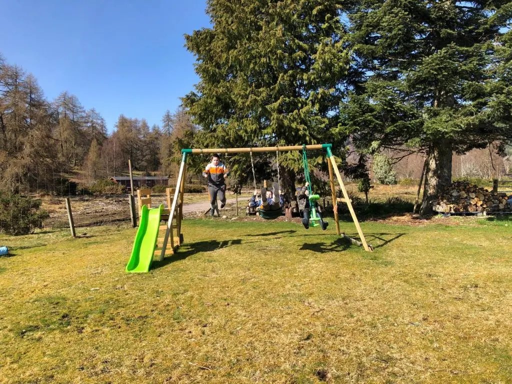 a man playing on a swing set in a yard at Juniper Hill Loch Achilty in Contin
