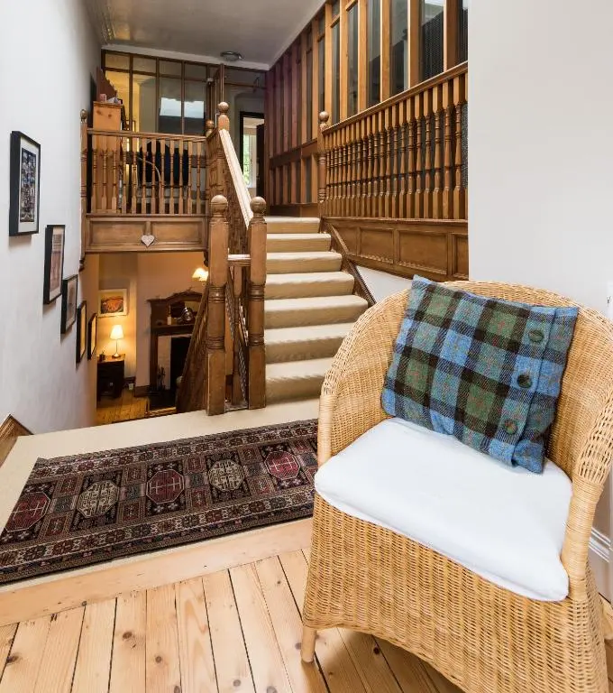 a living room with a wicker chair and stairs at Coig na Shee Guest House in Newtonmore