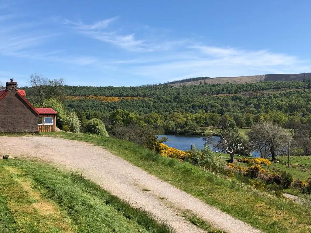 a dirt road next to a house and a lake at Nan's Cottage in Beauly