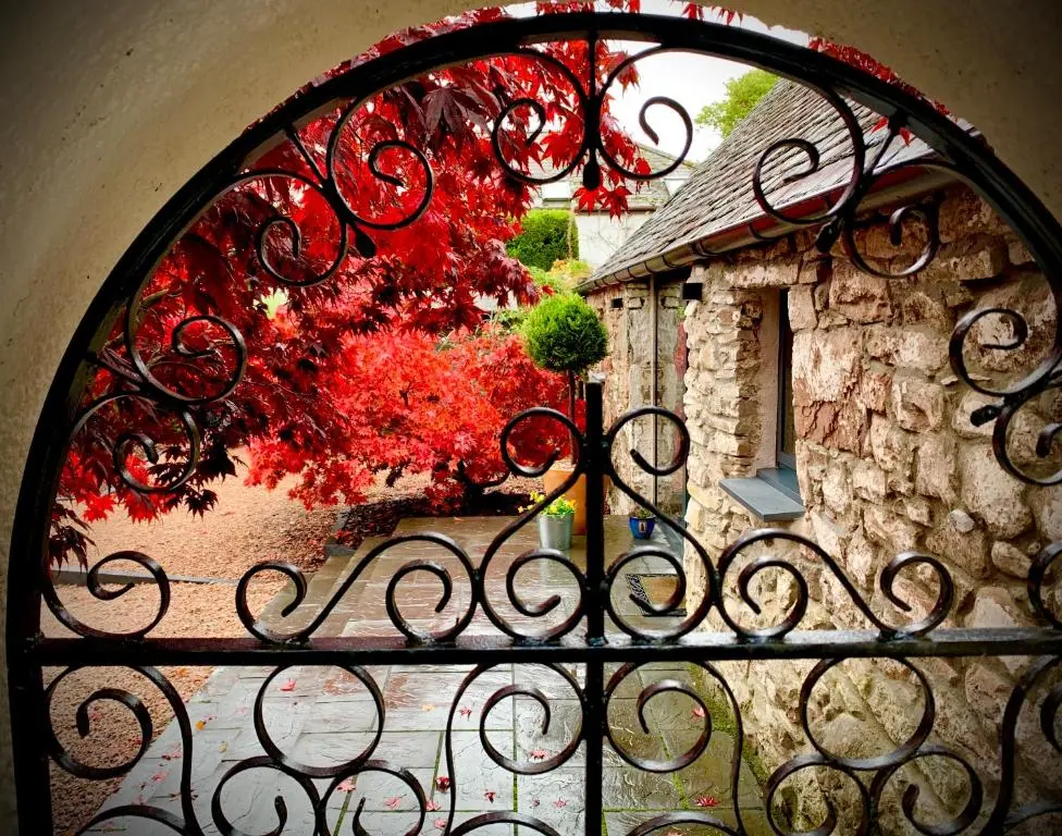 an iron gate with a window with a red tree at Balloan Cottage Cowshed in Inverness