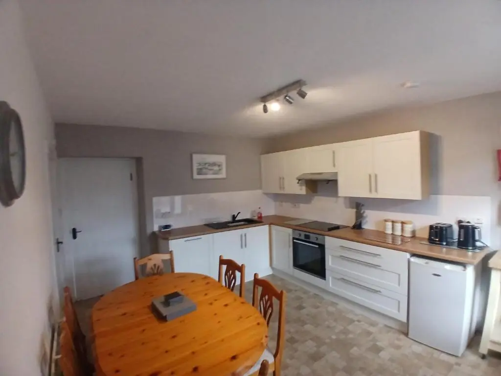 a kitchen with a wooden table and a kitchen with white cabinets at Mortlach Cottage in Dufftown