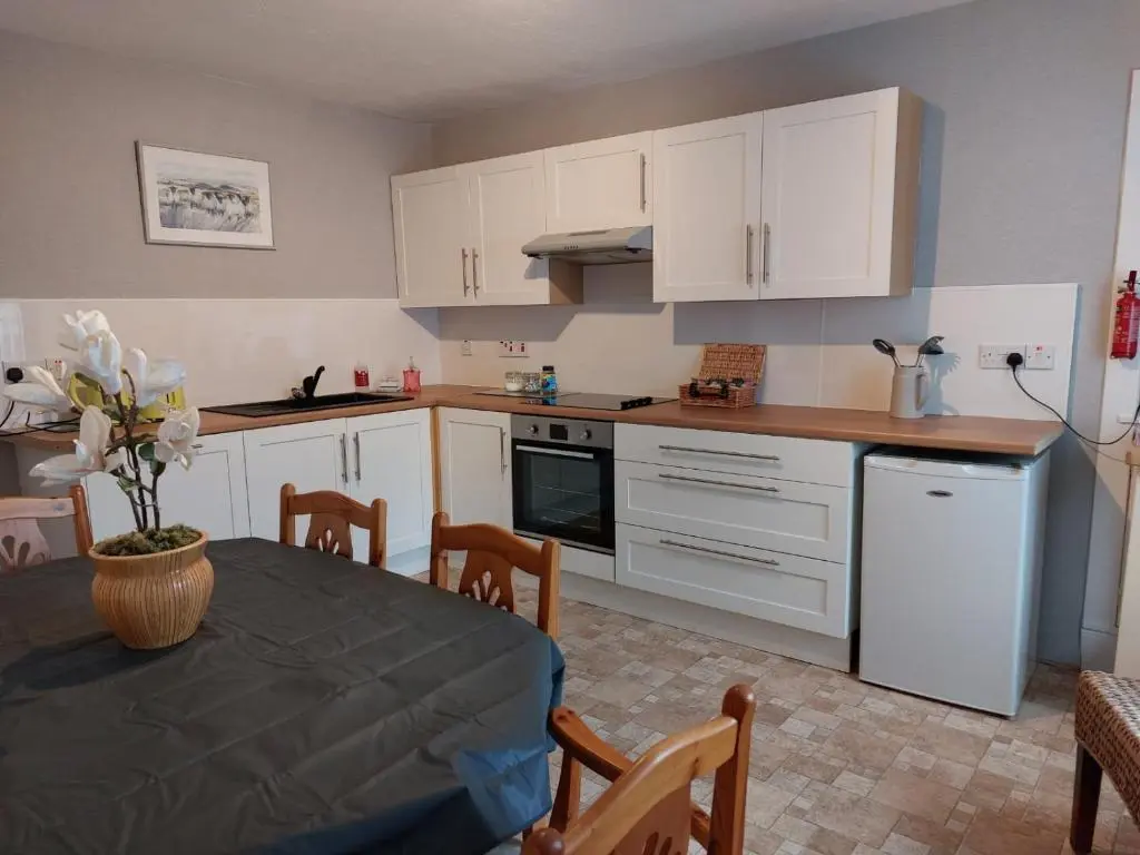a kitchen with white cabinets and a table with a vase at Mortlach Cottage in Dufftown