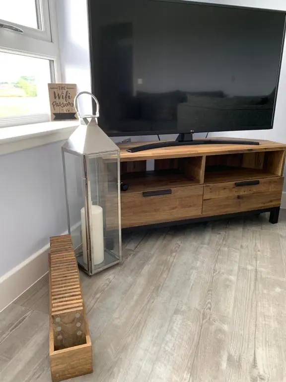 a living room with a large television on a wooden entertainment center at 23 C Allan Gardens in Dornoch