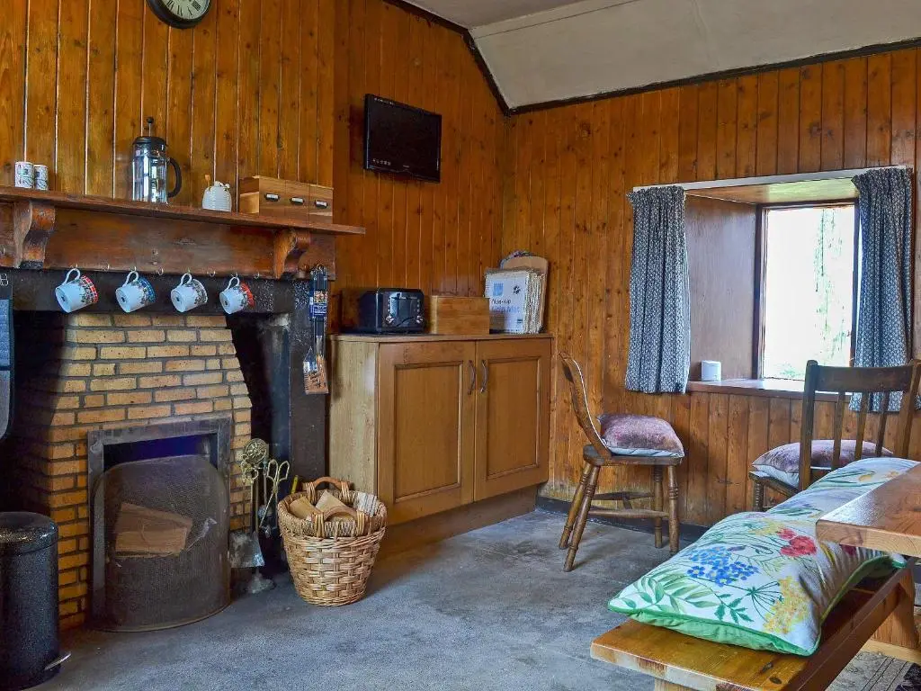 a living room with a fireplace and a table and chair at Mains Of Auchmedden Cottage in Pennan