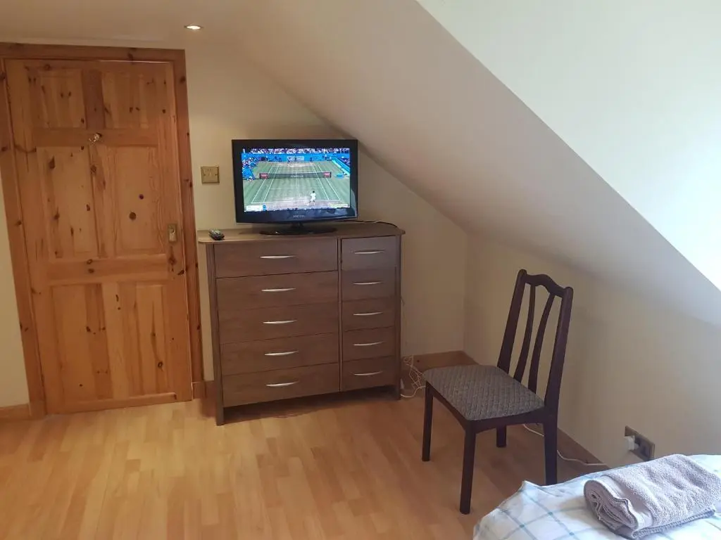 a bedroom with a tv on a dresser with a chair at Telford Road Apartment in Inverness