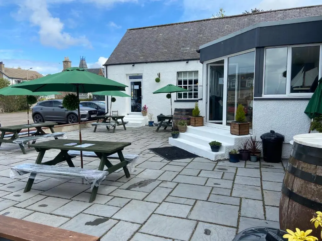 a patio with tables and umbrellas in front of a building at The 1645 Inn in Nairn