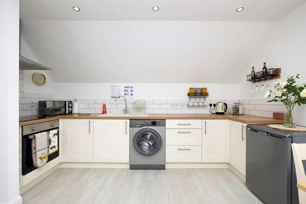 a kitchen with white cabinets and a washing machine at Pinewood Cottage Apartment & B&B Inverness in Inverness