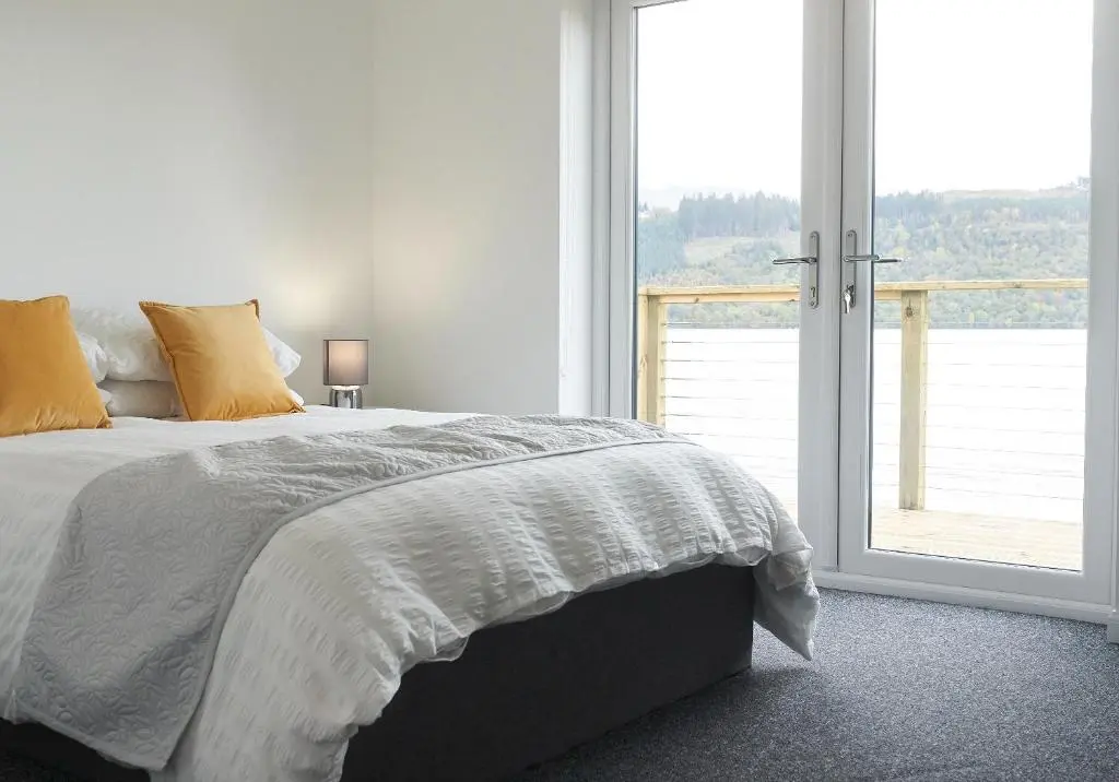 a white bedroom with a bed and a large window at Shoreland Lodges - Holly Lodge in Fort Augustus
