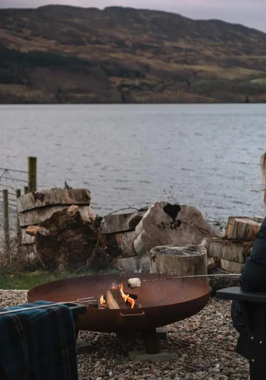 a fire pit sitting next to a body of water at Shoreland Lodges - Holly Lodge in Fort Augustus