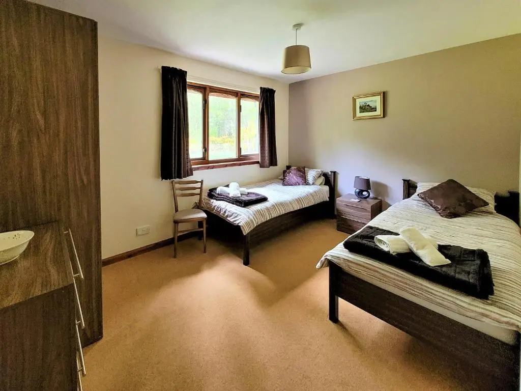 a bedroom with two beds and a chair in it at The Birches in Ardclach