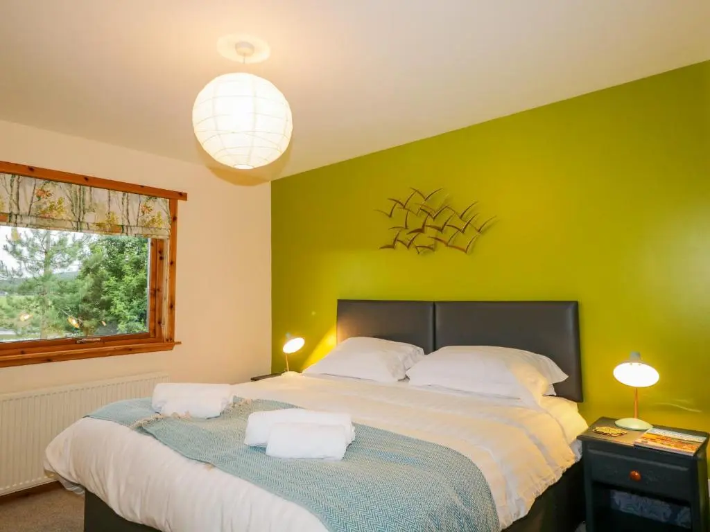 a bedroom with a large bed and a green wall at Ptarmigan in Carrbridge