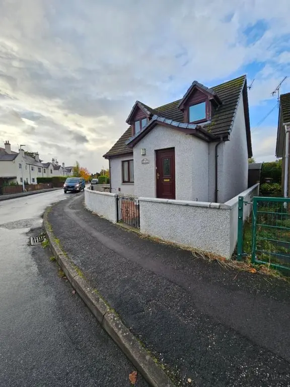 a white house with a red door on a street at The Cobblers in Inverness