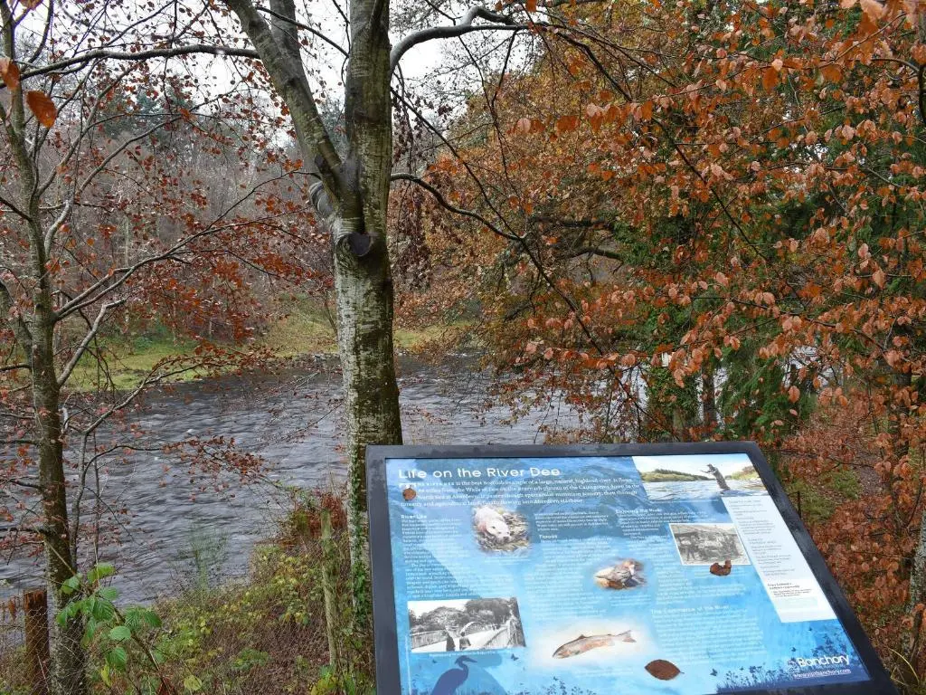 a sign in front of a river with trees at West Lodge in Banchory