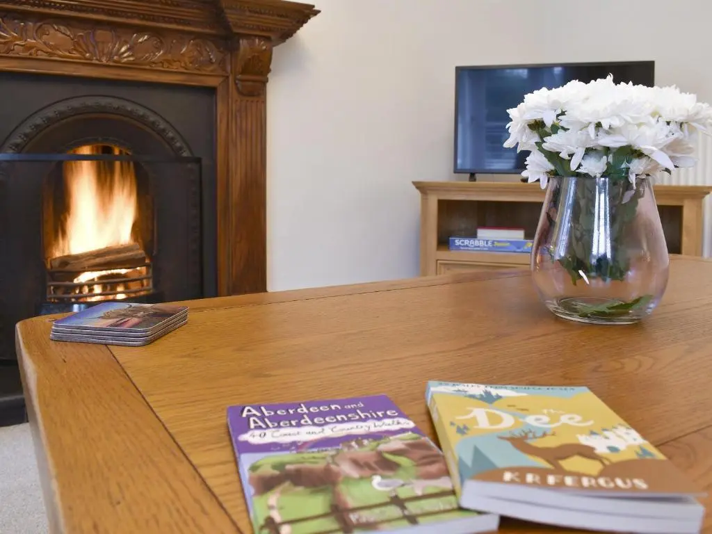 a table with a vase of flowers and a book at West Lodge in Banchory