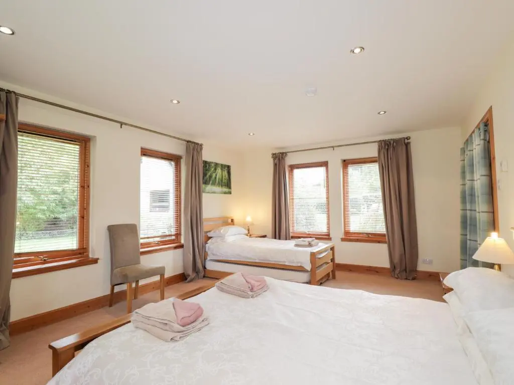 a bedroom with two beds and a desk and two windows at An Torr in Newtonmore