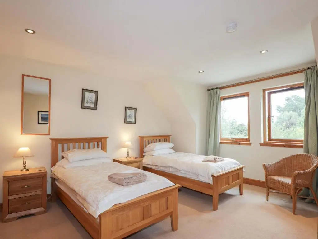 two beds in a room with two chairs and a window at An Torr in Newtonmore