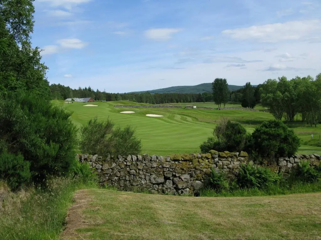 a view of a golf course with a stone wall at Apartment 20 Inchmarlo in Banchory