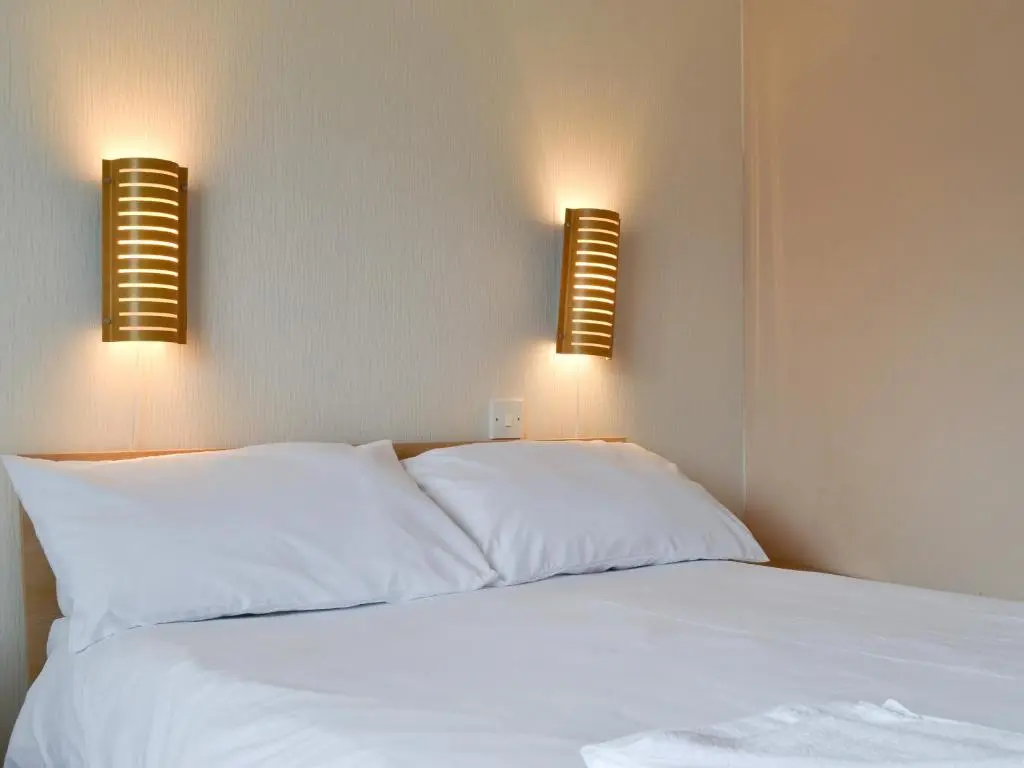 a bed with white sheets and two lights on the wall at Rowan Cottage in Aviemore