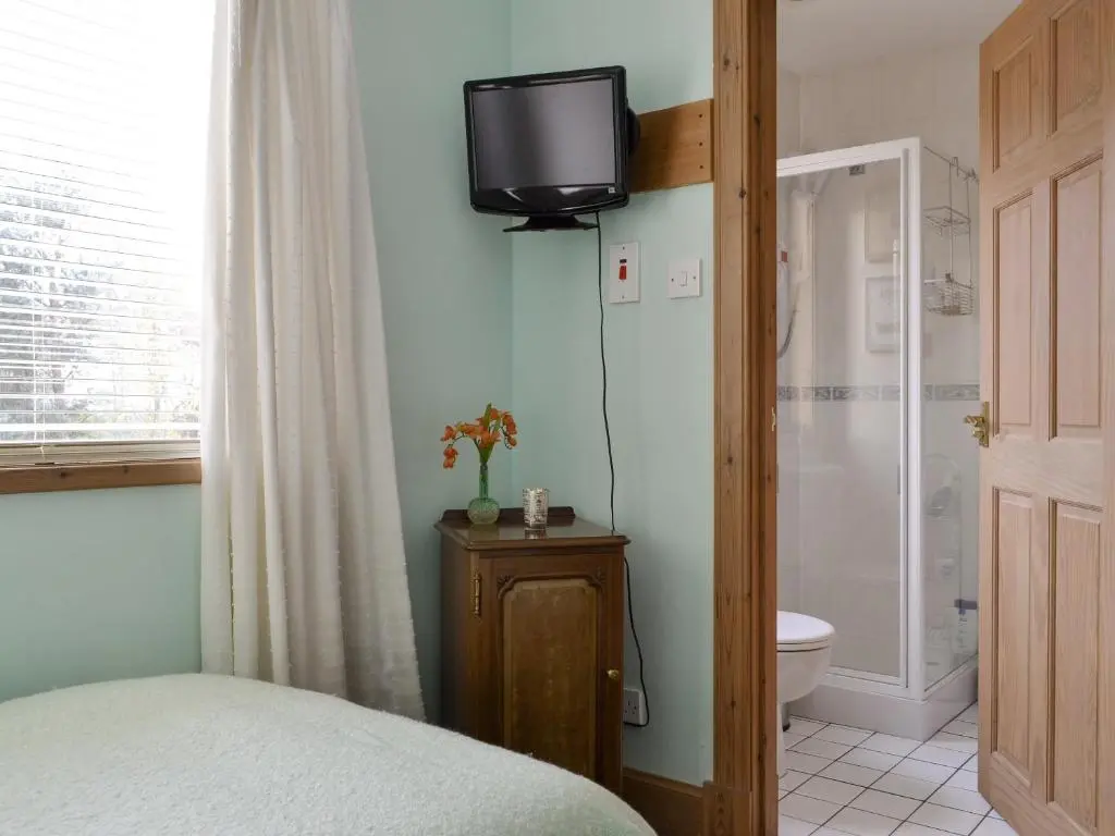 a bedroom with a bed and a television on the wall at Rowan Cottage in Aviemore