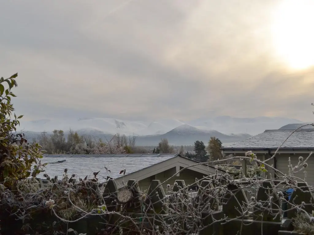 a house with snowy roofs and mountains in the background at Rowan Cottage in Aviemore