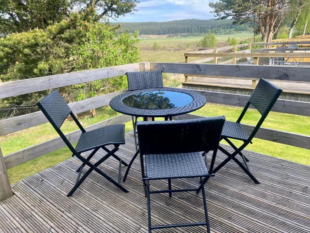 a table and chairs on a deck with a fire pit at Bynack Lodge in Boat of Garten